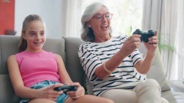 Video of cute granddaughter teaching her grandmother to play video games on the console on sofa at home