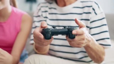 Video of cute granddaughter teaching her grandmother to play video games on the console on sofa at home