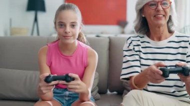 Video of cute granddaughter teaching her grandmother to play video games on the console on sofa at home