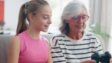 Video of cute granddaughter teaching her grandmother to play video games on the console on sofa at home
