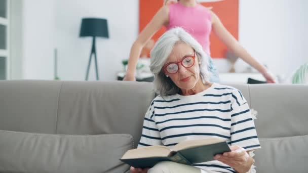 Видео Добрая Пожилая Женщина Читает Книгу Время Внучка Обнимает Сзади — стоковое видео
