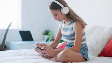 Yatakta oturmuş akıllı telefonuyla müzik dinleyen güzel bir genç kızın videosu..
