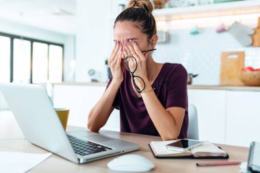 Evde dizüstü bilgisayarla çalışan stresli iş kadını endişeli, yorgun ve bunalmış görünüyor..