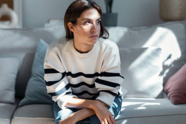 Evdeki kanepede otururken sorunlarını düşünen depresif bir genç kadın..