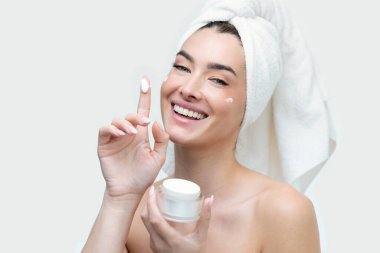 Portrait of a beautiful young natural girl without makeup applies a cream to a face with fingers. clipart