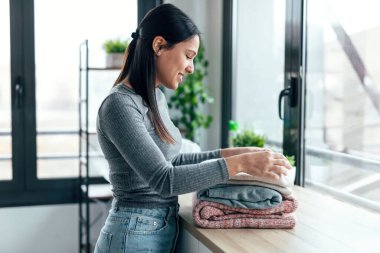 Shot of young woman folding clothes on a table at home