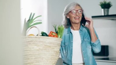 Evde, mutfakta akıllı telefonla konuşan mutlu olgun bir kadının videosu..
