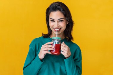 Sarı üzerine izole edilmiş kırmızı smoothie içen gülümseyen kadın portresi.