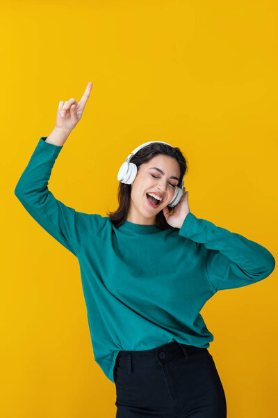 Portrait of smiling woman dancing and listening to music with headphones isolated on yellow
