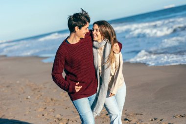 Genç ve güzel bir çiftin kumsalda soğuk bir kışın tadını çıkardığı bir çekim..