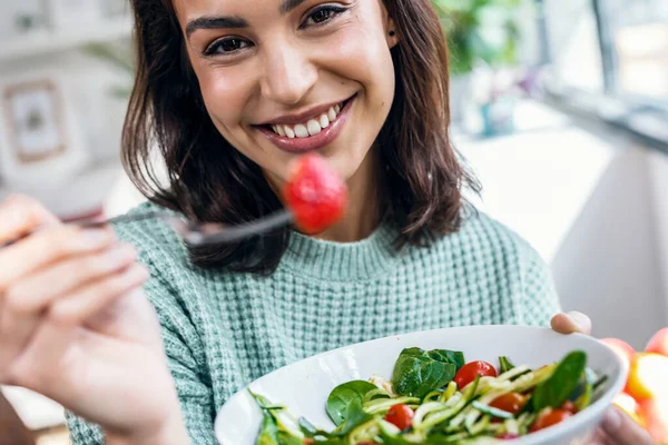 Laukaus Kaunis Hymyilevä Nainen Syö Terveellistä Salaattia Istuessaan Pöydällä Kotona — kuvapankkivalokuva