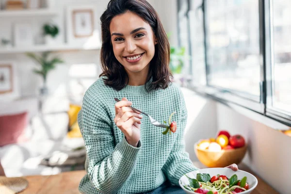 美しい笑顔の女性のショット自宅でテーブルの上に座って健康的なサラダを食べる — ストック写真