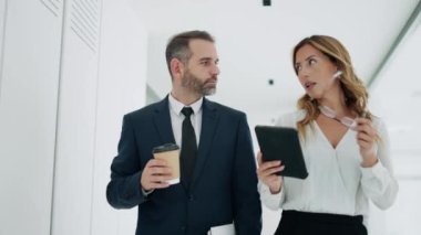 Modern bir girişimde konuşurken ve yürürken dijital tabletle çalışan çekici iş çifti videosu.