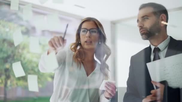現代的なオフィスで一緒に議論しながら オフィスのガラス板でステッカーに書いて成功したビジネスカップルチームのビデオ — ストック動画