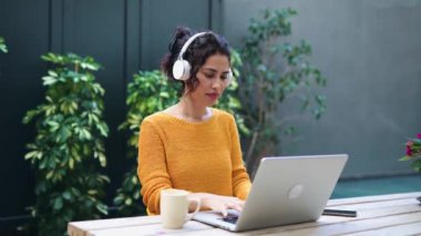 Kulaklıklı güzel bir kadının laptopla çalışırken kahve içerken bir kafede oturduğu video.