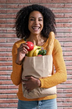 Mutlu güzel bir kadının elinde karton bir çantayla evde sağlık alışverişi yaptığı bir fotoğraf.