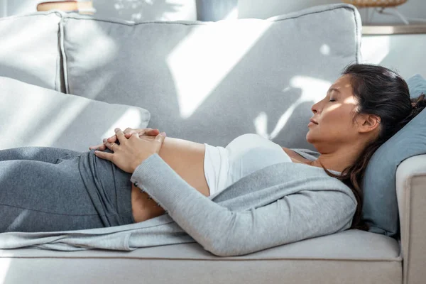 自宅でソファに横たわっている間に彼女の腹に触れる美しいです妊娠中の女性のショット — ストック写真