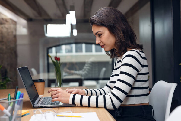 Shot of architect engineer woman working with laptop while studying the blueprints in a modern office.
