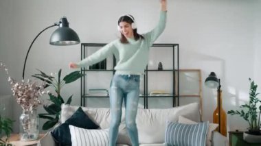 Evdeki oturma odasında kanepede dans ederken akıllı telefonlu müzik dinleyen komik bir kadının videosu.