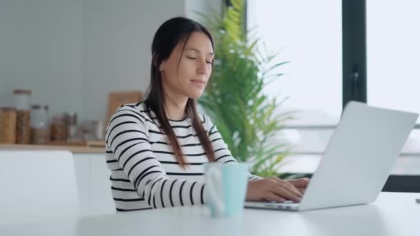 自宅のキッチンでノートパソコンで働く笑顔の若い女性のビデオ — ストック動画
