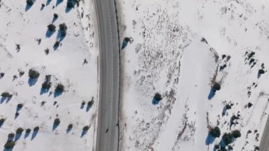 Karlı bir dağın kıvrımlarında dolaşan beyaz bir arabanın insansız hava aracı görüntüsü.