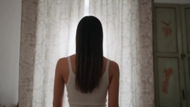 Güzel bir kızın sabah erkenden pencerenin önünde jaluzi açarken videosu.