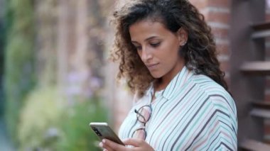 Güzel bir kadının parkta oturup kahve içerken cep telefonunu kullanmasının videosu.
