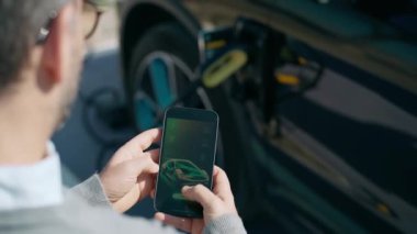 Elektro arabayı şarj ederken cep telefonu kullanan adamın yakın çekim videosu.