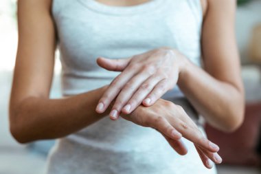 Evde genç bir kadının ellerine krem sürerken yakın plan.