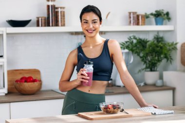 Shot of athletic woman drinking healthy protein shake in the kitchen at home clipart