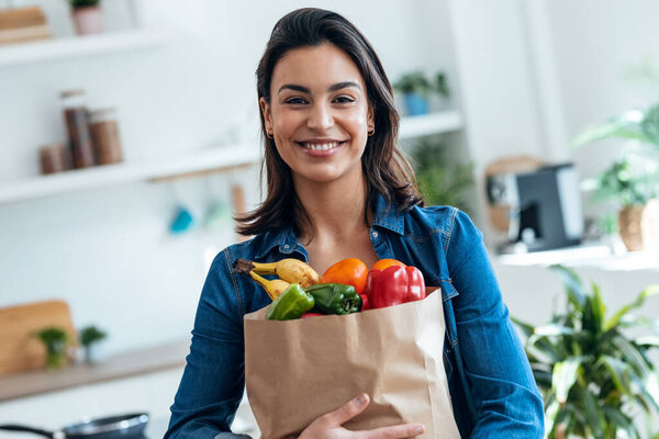 Shot of happy beautiful woman holding cardboard bag with health shopping in kitchen at home