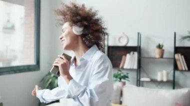 Güzel genç bir kadının kulaklıkla müzik dinlerken evdeki oturma odasında akıllı telefonuyla şarkı söyleyen insanların videosu..