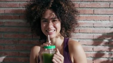 Evdeki oturma odasında duran sağlıklı yeşil smoothie içen mutlu kadının videosu..