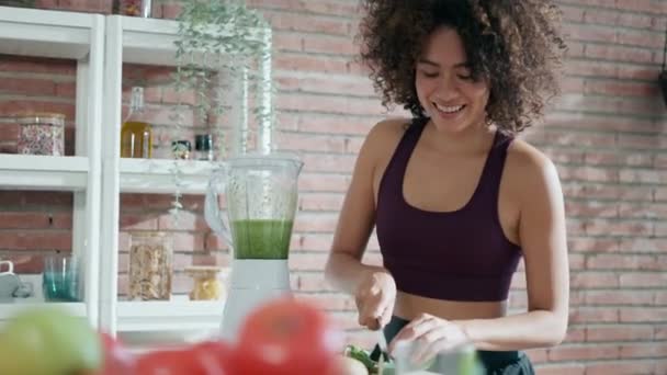 家でキッチンで野菜の緑スムージーを作るスポーティーな若い女性のビデオ — ストック動画