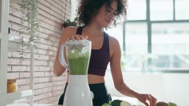 家でキッチンで野菜の緑スムージーを作るスポーティーな若い女性のビデオ — ストック動画