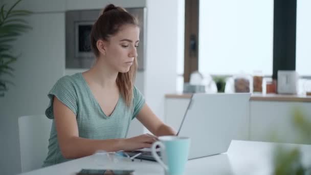 自宅のキッチンでコーヒーを飲みながらラップトップで作業しているかなり若い女性のビデオ — ストック動画