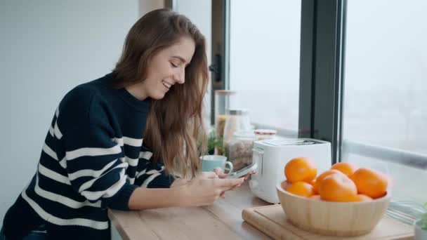 朝のキッチンで携帯電話を使いながら美しい若い女性がコーヒーを飲むビデオ — ストック動画