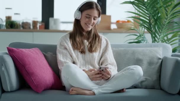 Video Beautiful Woman Listening Music While Using Smartphone Sitting Sofa — стоковое видео