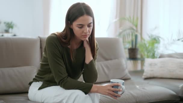 自宅のソファでコーヒーを飲みながら 自分の問題を考える落ち込んだ若い女性のビデオ — ストック動画