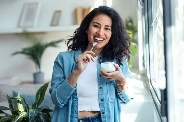 Evdeki Oturma Odasında Dikilirken Yoğurt Yiyen Mutlu Bir Kadın — Stok fotoğraf