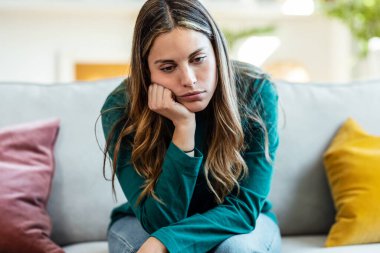 Evdeki kanepede oturup düşünen ve endişelenen güzel bir genç kadın..