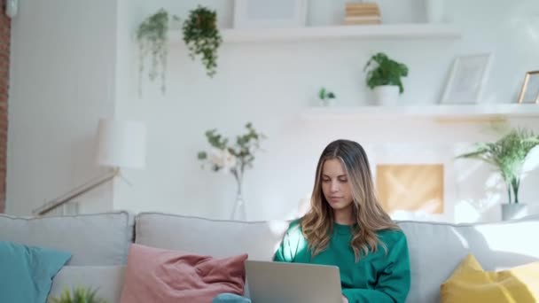 一个漂亮善良的女人坐在客厅的沙发上与笔记本电脑一起工作的视频 — 图库视频影像