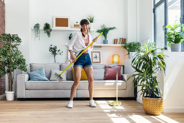 stock image Shot of funny motivated woman dancing and listening to music with headphones while sweeping the house