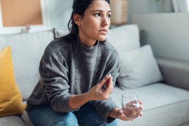 Evdeki kanepede otururken depresyonda olan üzgün kadının haplarını içmesi..