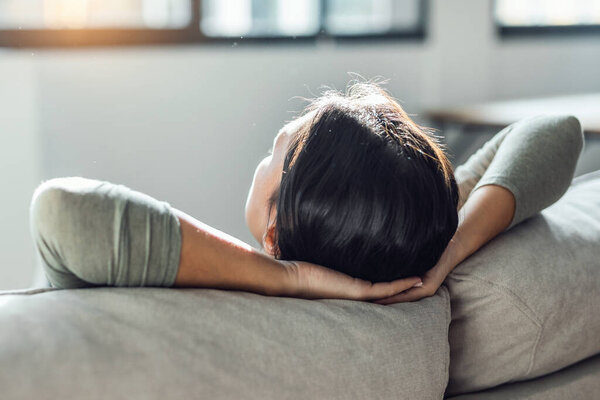 Shot of young tired woman relaxing while lying on couch in living room at home.
