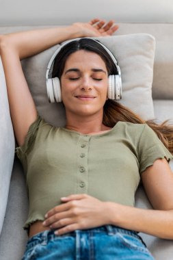 Evde kanepede uzanmış kulaklıkla müzik dinleyen güzel bir kadın.