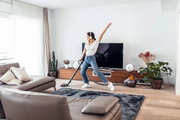 リビングルームの床を掃除しながら音楽を聴いて踊る若い幸せな女性のショット — ストック写真