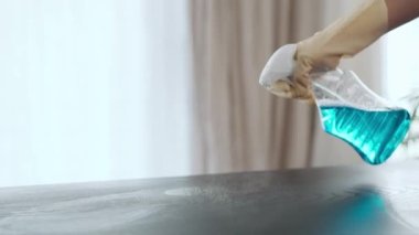 Eldivenli genç kadın ellerinin masayı spreyle temizlerken çekilmiş videosu.