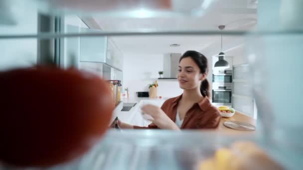 自宅のキッチンの冷蔵庫からいくつかの健康的な食べ物を取る美しい若い女性のビデオ — ストック動画