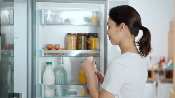自宅のキッチンの冷蔵庫から健康なピンクのスムージーを飲む美しい若い女性のビデオ — ストック動画